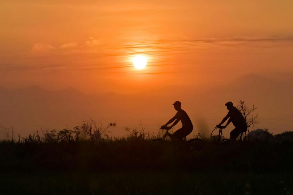 Silhouettes de deux personnes en randonnée cyclotouristique, avec couché de soleil en arrière plan.